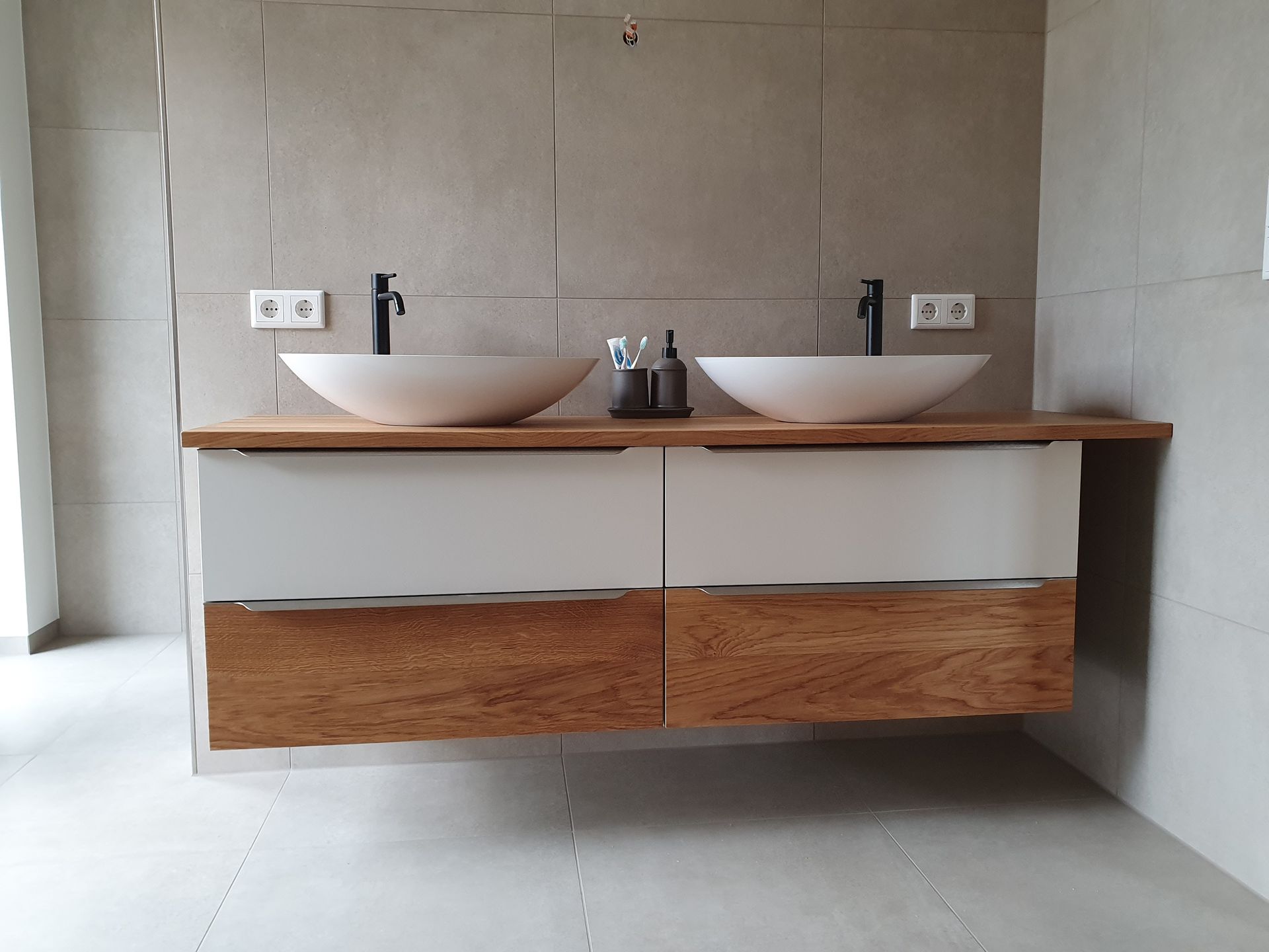 Schwebender Badezimmerwaschtisch mit weißen Waschbecken, schwarzen Wasserhähnen und Holzschubladen.