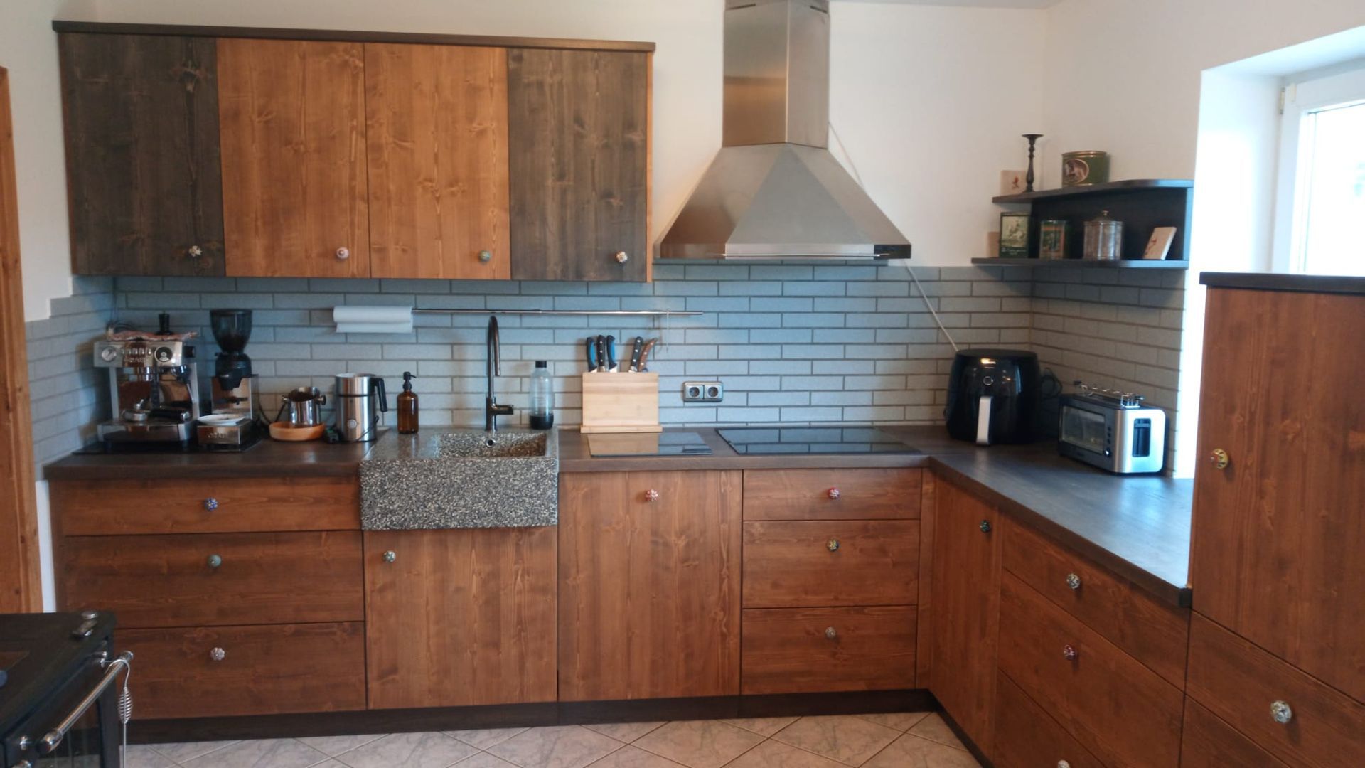 Küchenschränke und Arbeitsplatte aus Holz. Dunstabzugshaube aus Edelstahl über dem Herd mit weißer Ziegelrückwand.