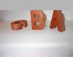 Letras de madera que forman la palabra “BA” junto a un anillo enrollado de color cobre sobre una superficie blanca.