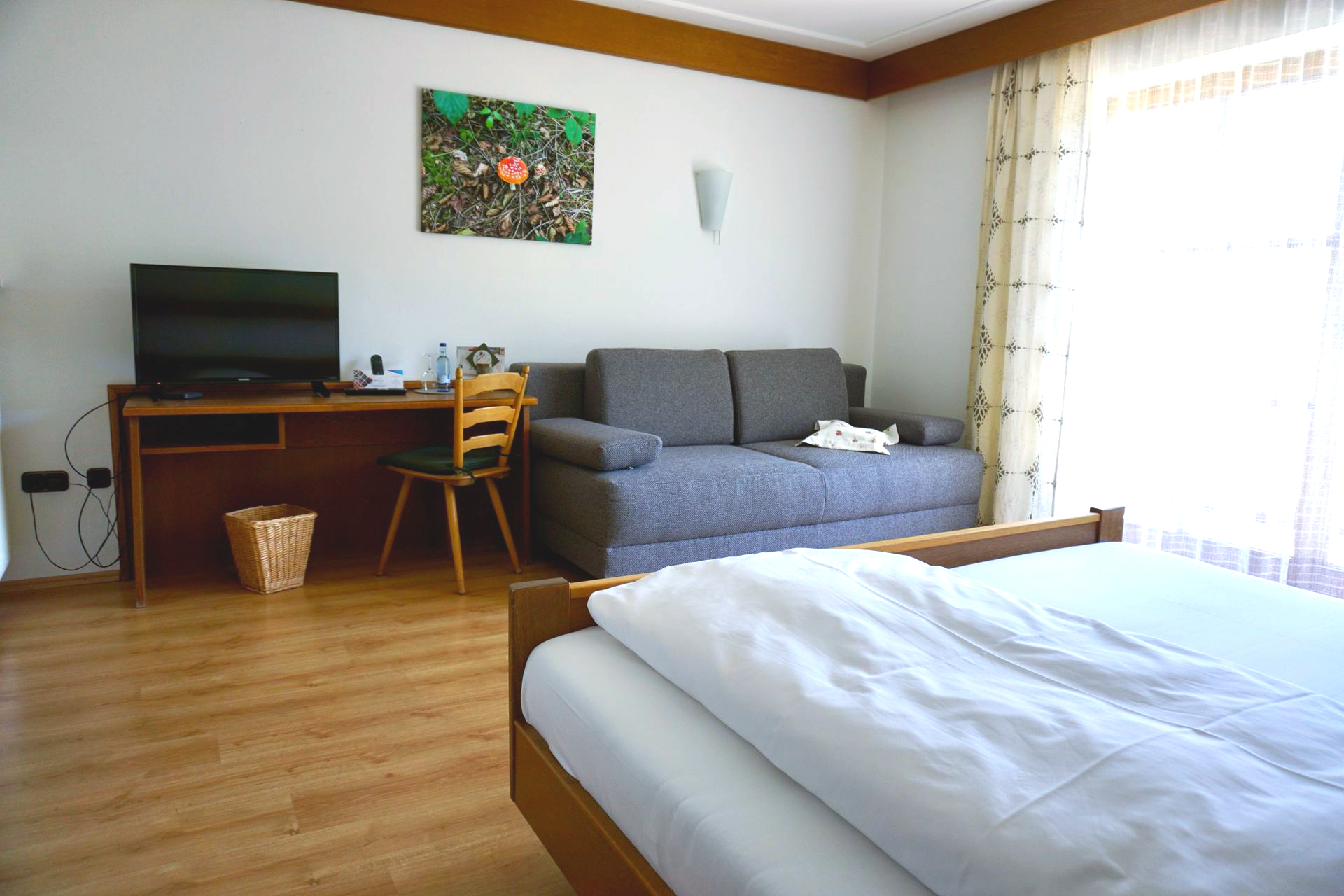 Helles Hotelzimmer mit Doppelbett, Sofa, TV und großem Fenster.