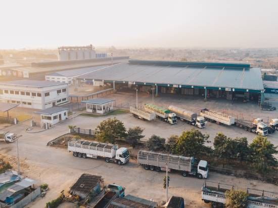 Vista aérea de um grande complexo industrial com armazéns, caminhões e reboques estacionados ao pôr do sol.