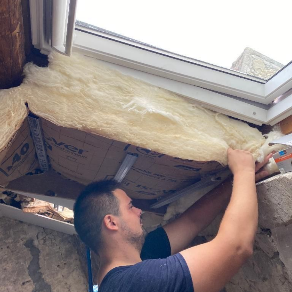 Un homme installe de l'isolant dans un cadre de fenêtre.
