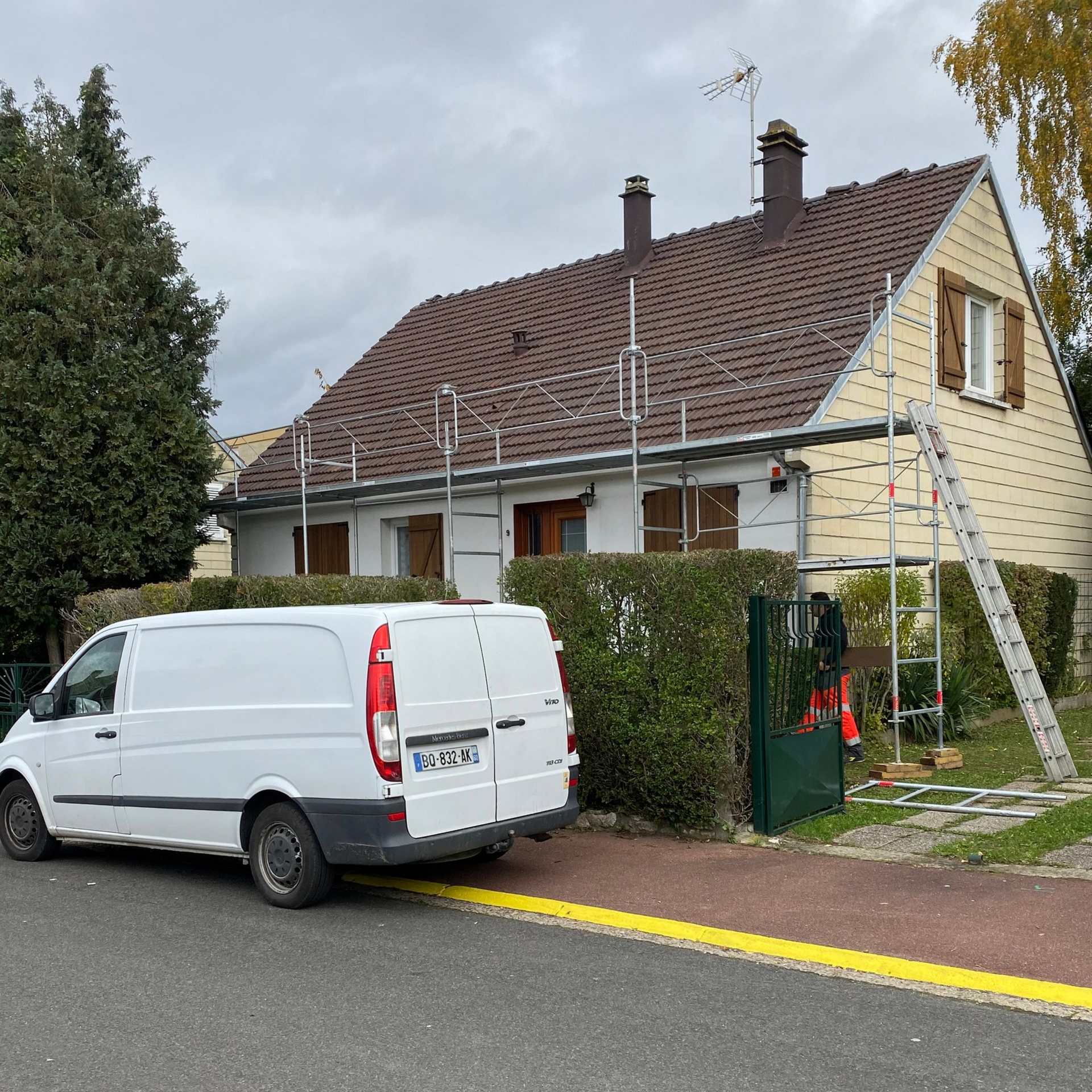 Une camionnette blanche est garée près d'une maison où se trouvent un échafaudage et une échelle.
