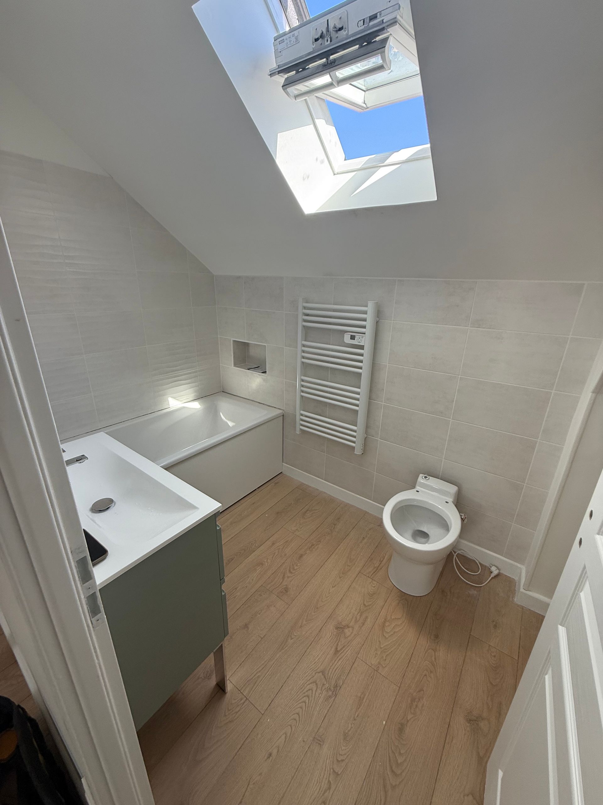 Salle de bains avec puits de lumière, baignoire, toilettes, meuble-lavabo et sèche-serviettes.
