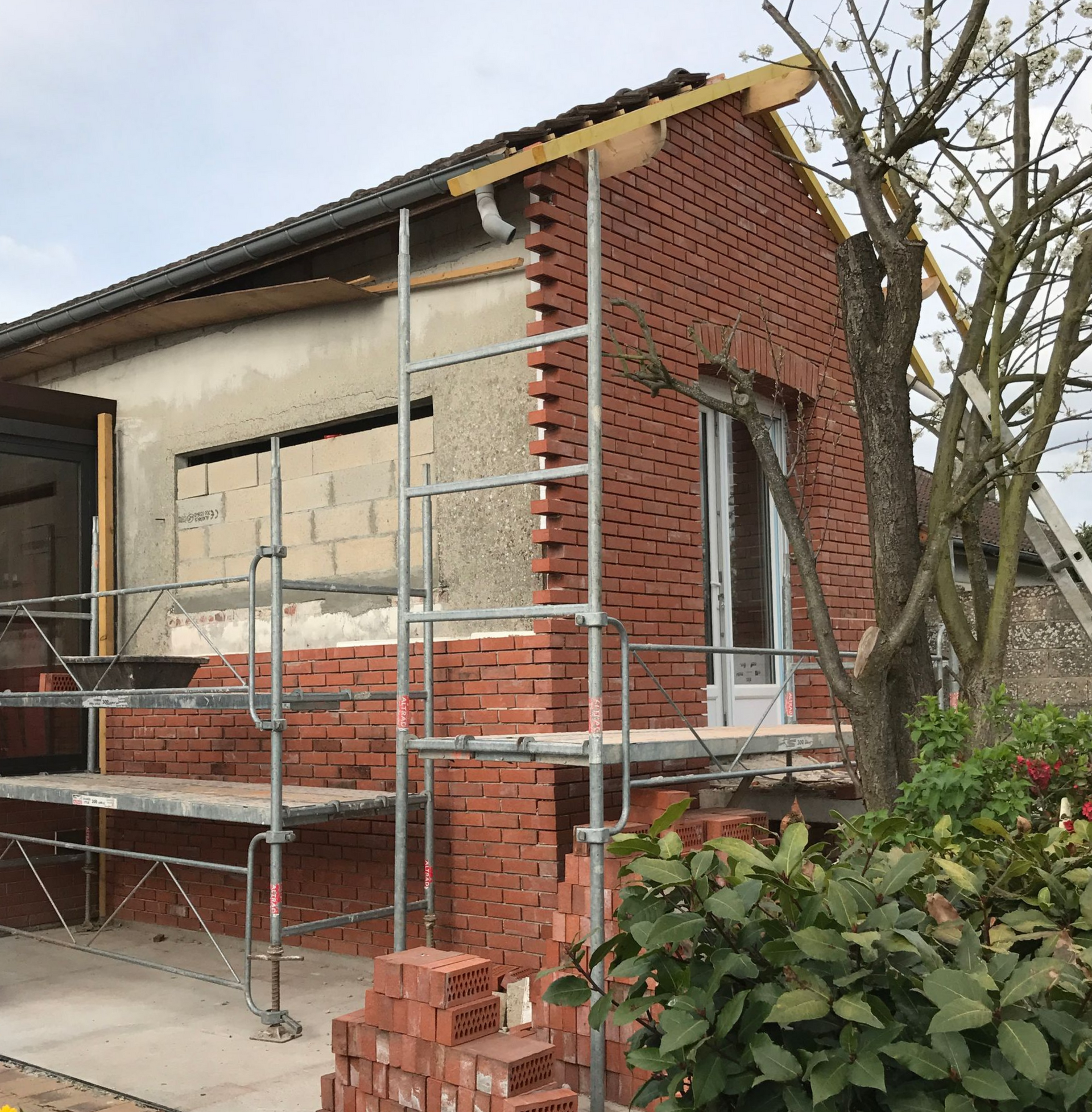 Construction d'une maison en briques, avec échafaudages et briques empilées visibles.