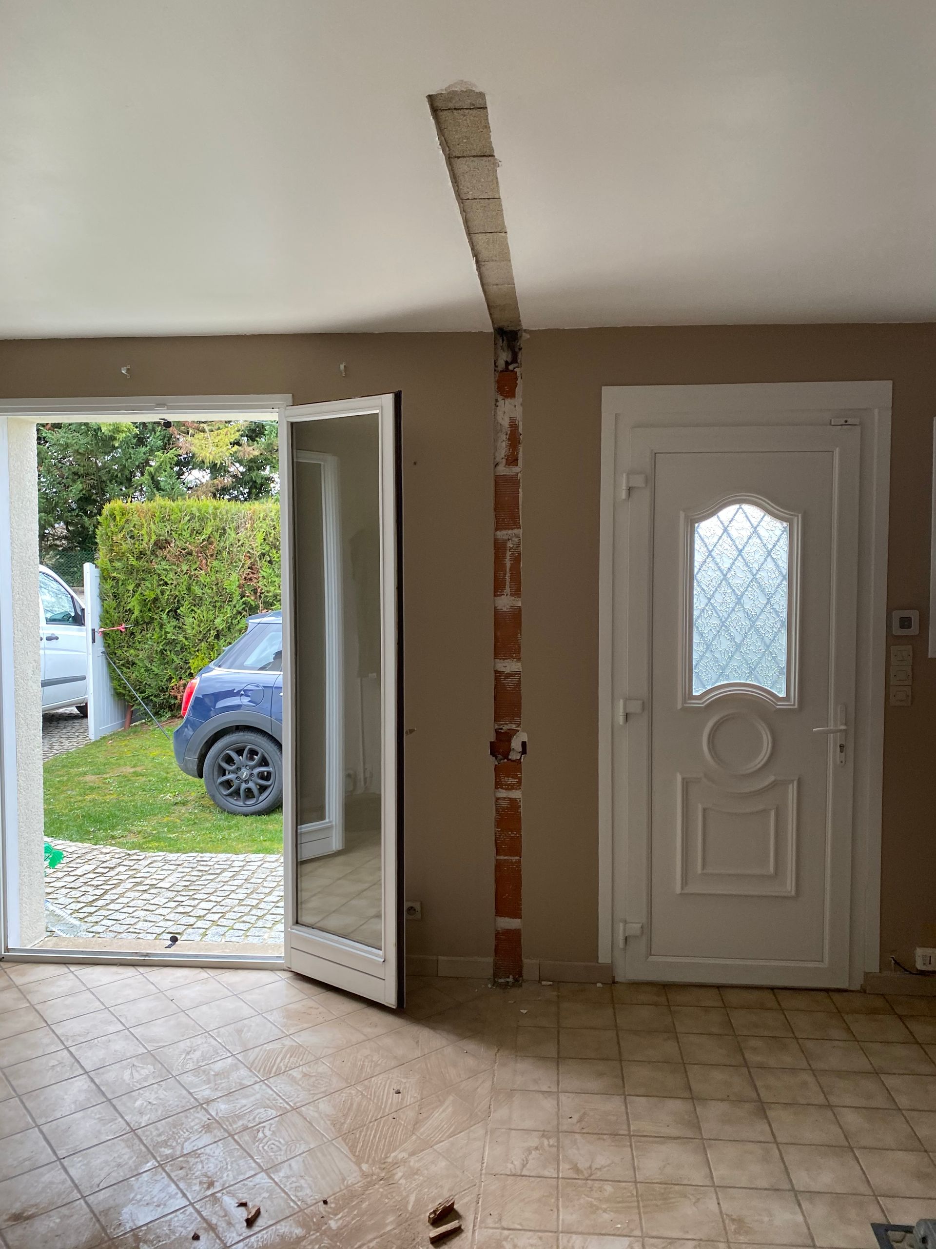 Démolition d’un mur dans une pièce avec une porte donnant sur l’extérieur et une porte blanche fermée.