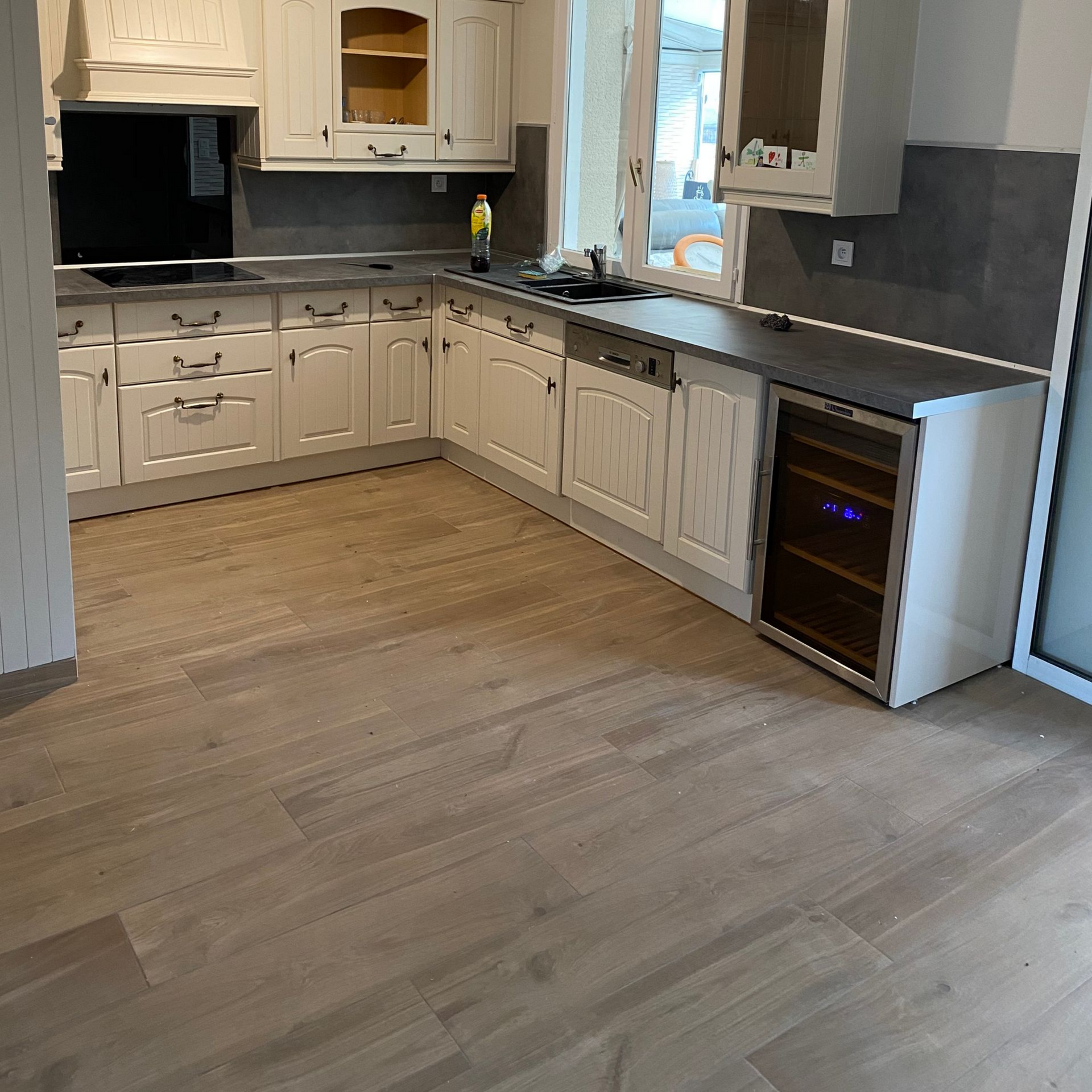 Cuisine avec parquet clair, placards blancs, plans de travail gris et cave à vin intégrée.