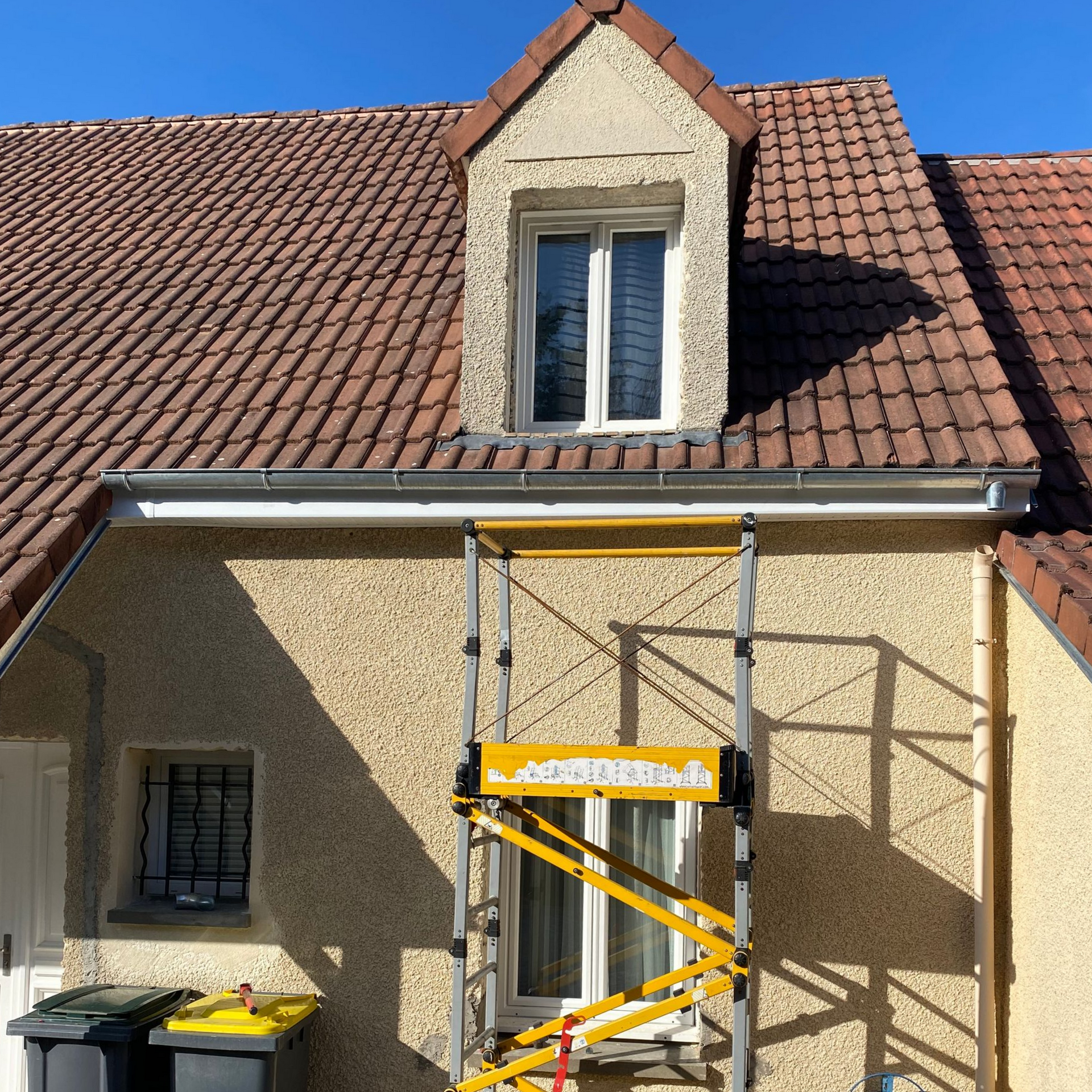 Une lucarne sur un toit de tuiles. Un échafaudage se dresse devant la fenêtre.