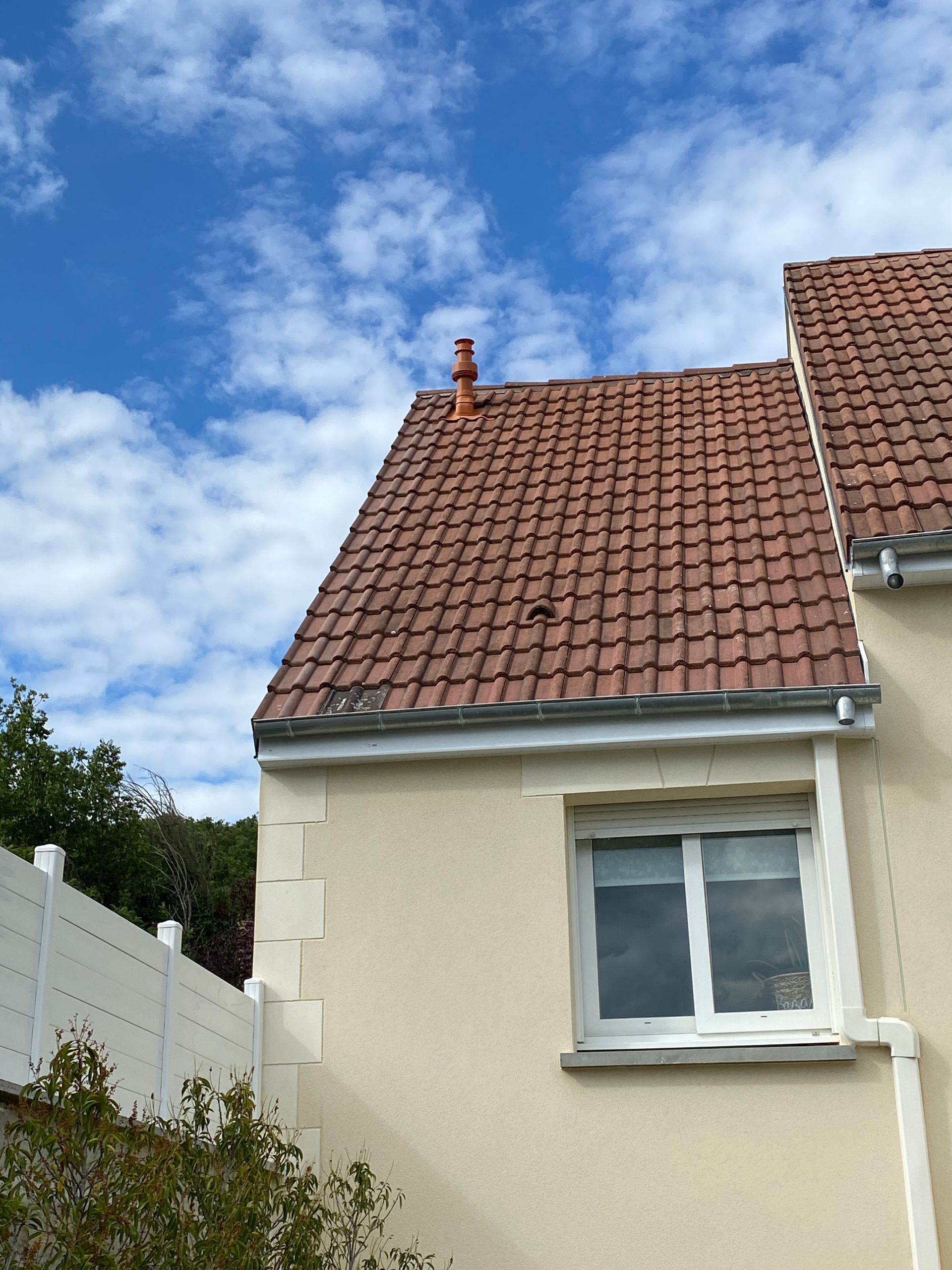 Toit de tuiles rouges sur une maison couleur crème.