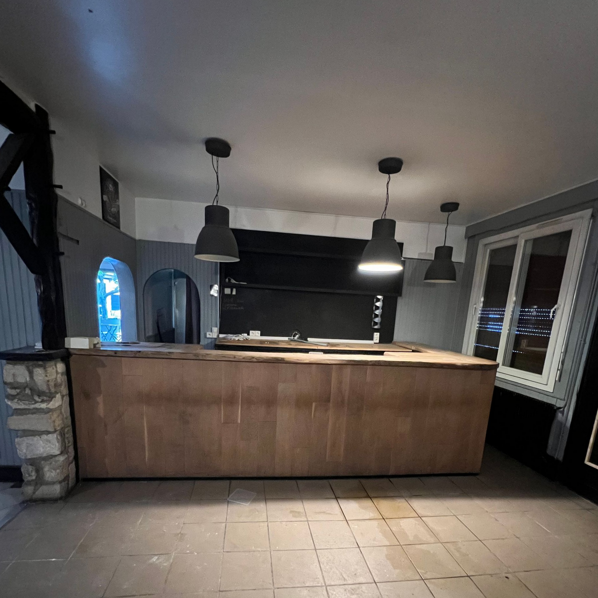 Cuisine avec un bar en bois et trois suspensions lumineuses.