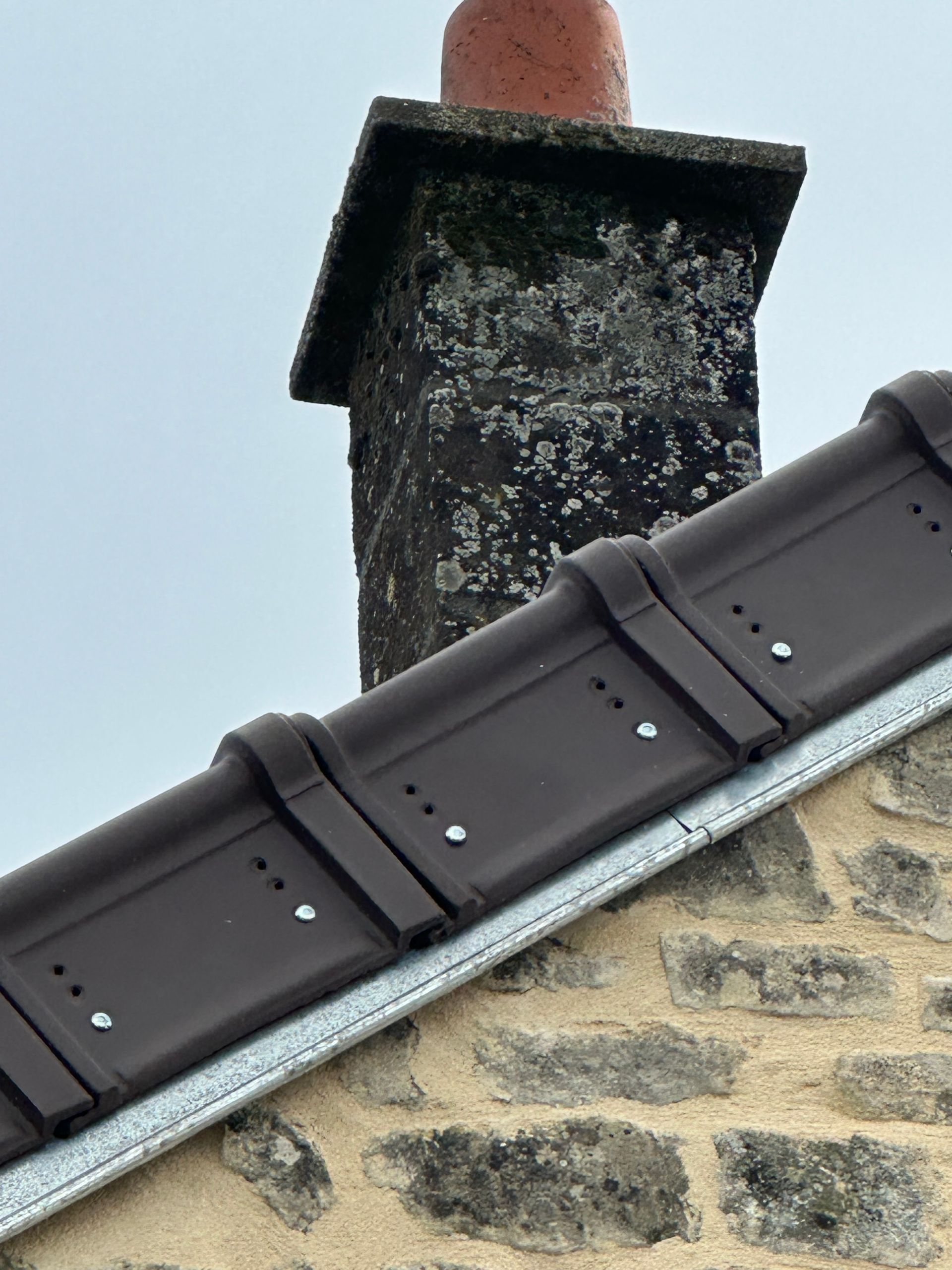 Des tuiles de toit brun foncé, bordées de solins métalliques.