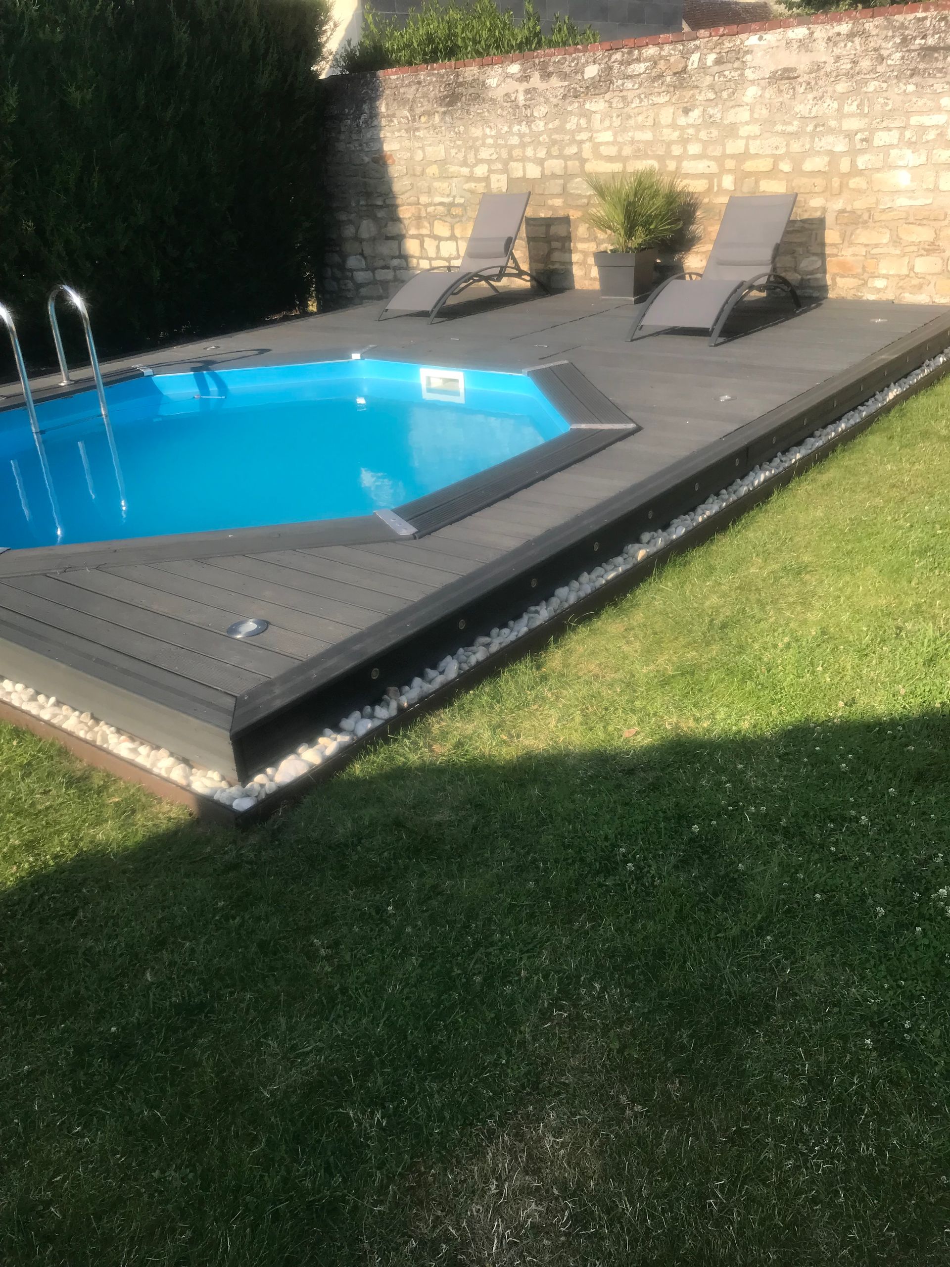 Un jardin avec une piscine bleue entourée d'une terrasse en bois sombre.