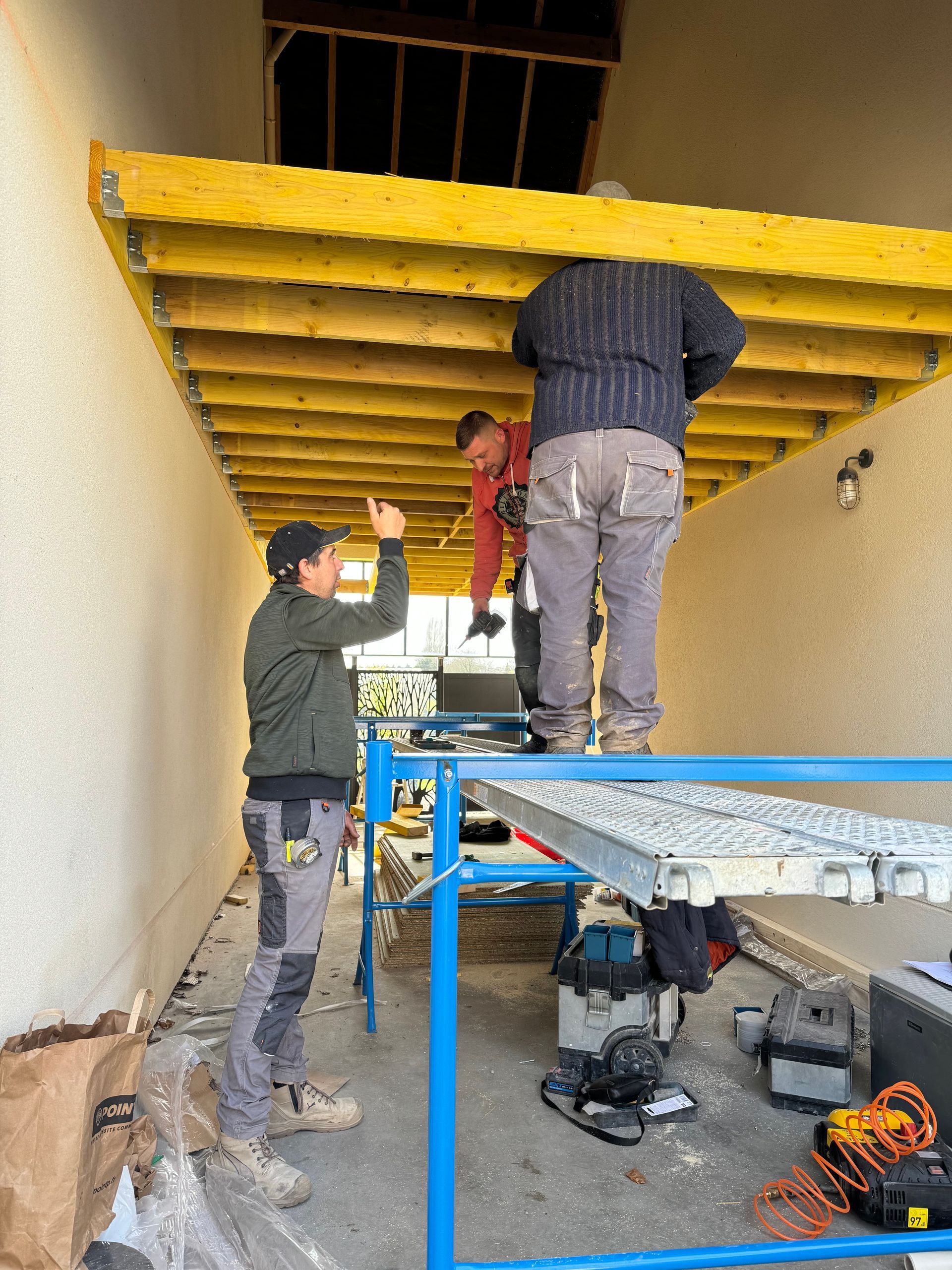 Trois ouvriers du bâtiment travaillent sous un plafond.