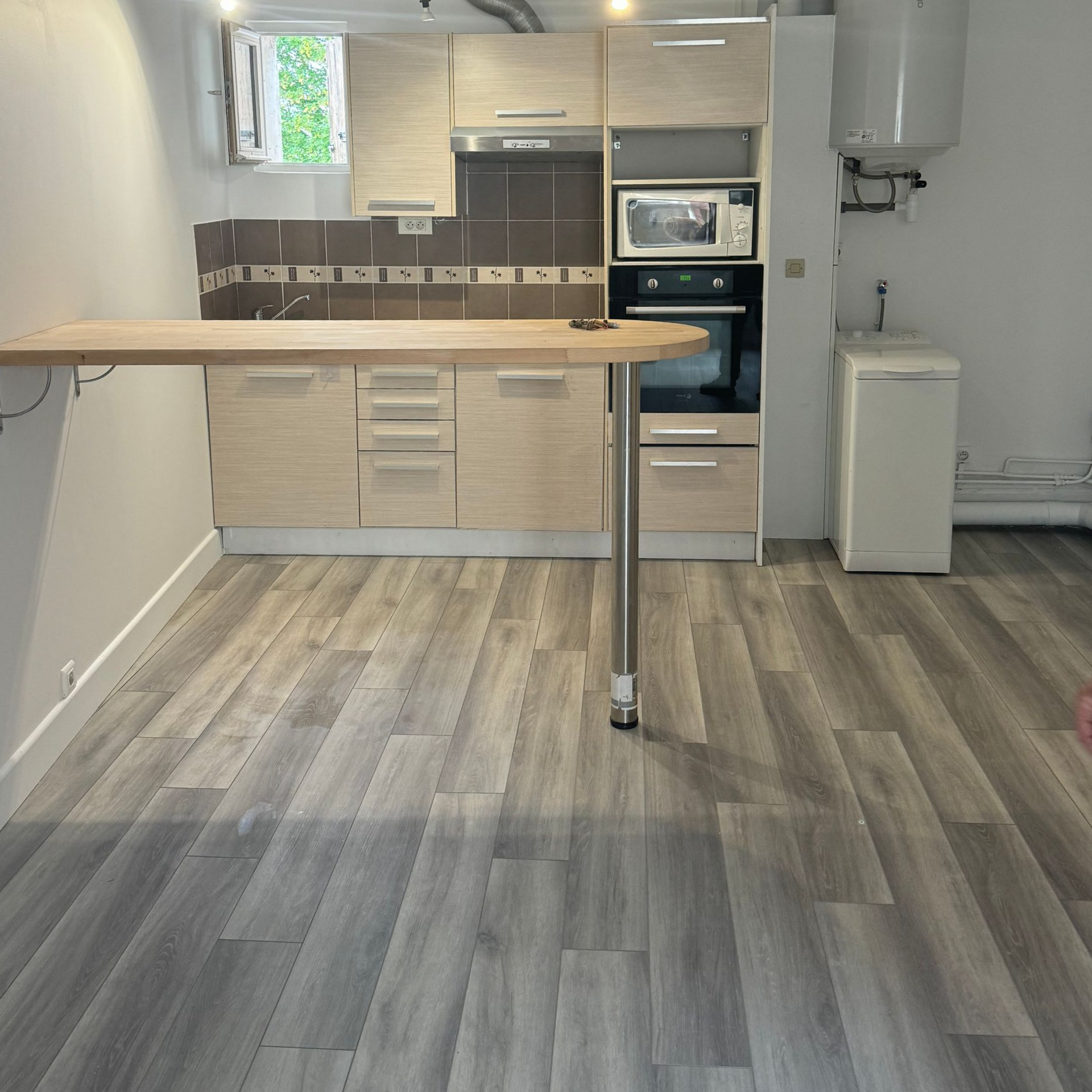 Petite cuisine avec sol imitation bois, placards clairs et table rabattable.