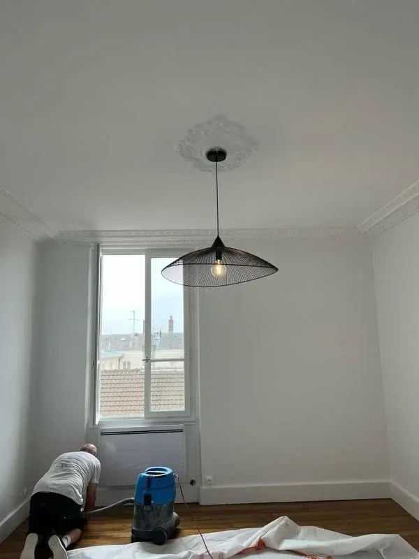 Pièce vide avec parquet, fenêtres et cheminée en marbre.