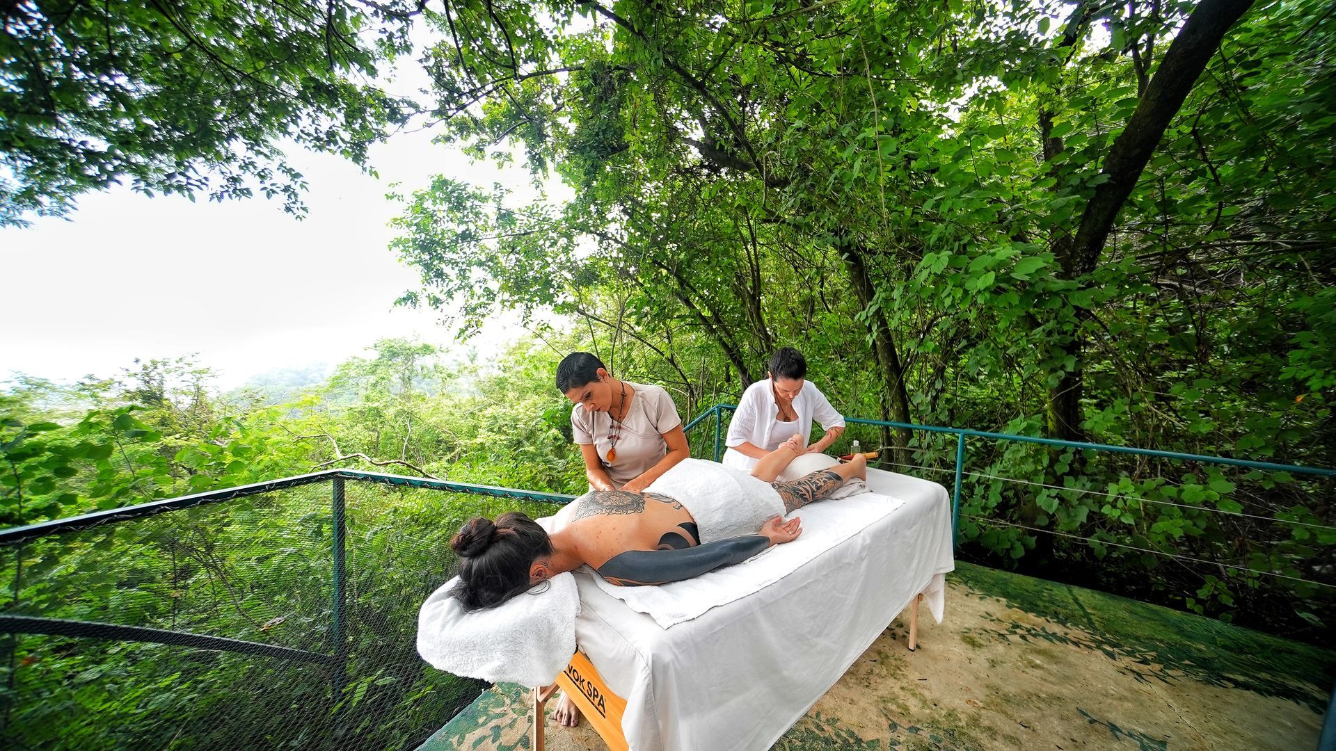 A woman is getting a massage on a table in the woods.