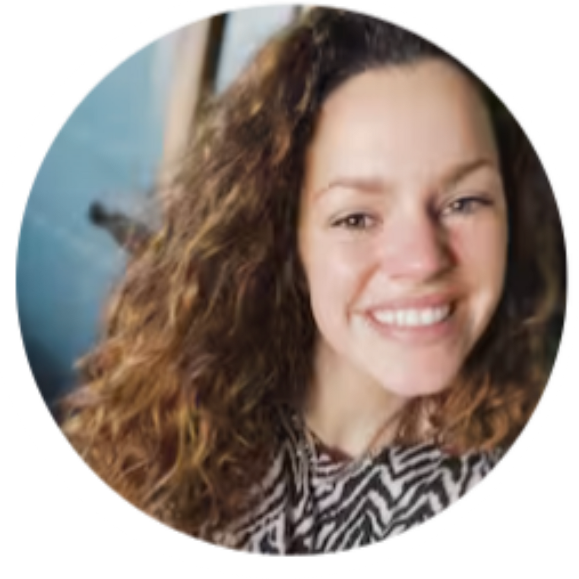 Woman with curly brown hair smiles. She is wearing a black and white patterned shirt.