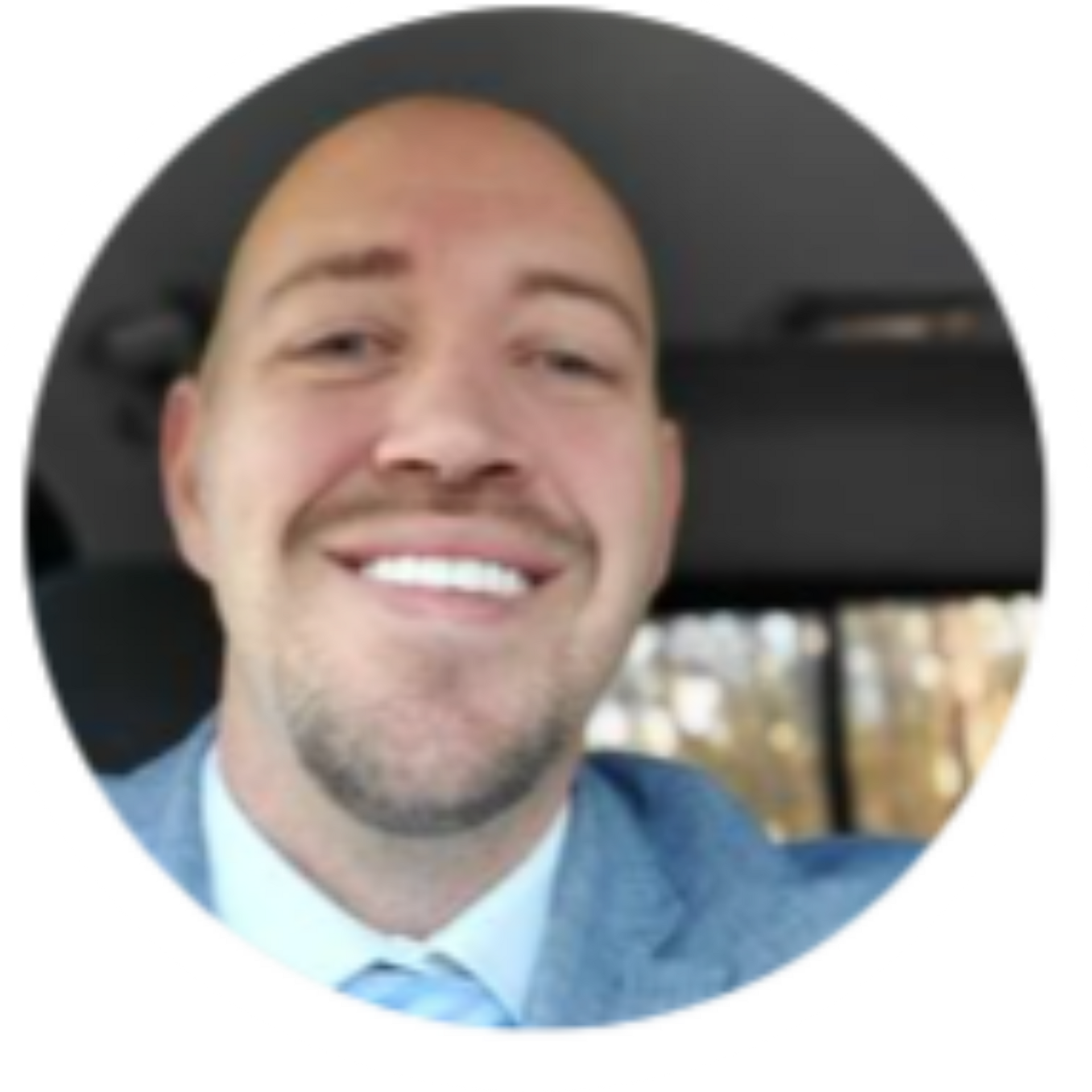 Man with a shaved head and a light blue blazer smiles widely.