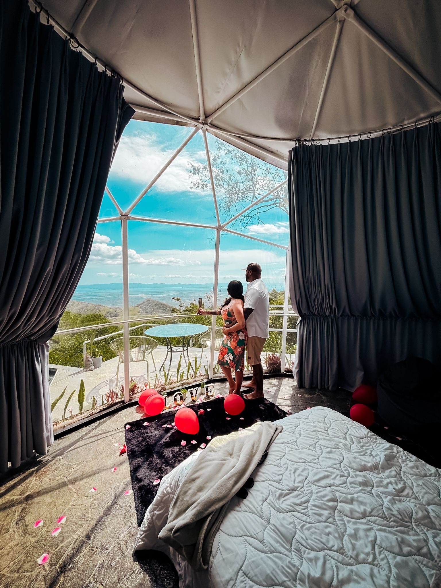 Couple in dome with view, red balloons. They are looking out at scenic landscape.