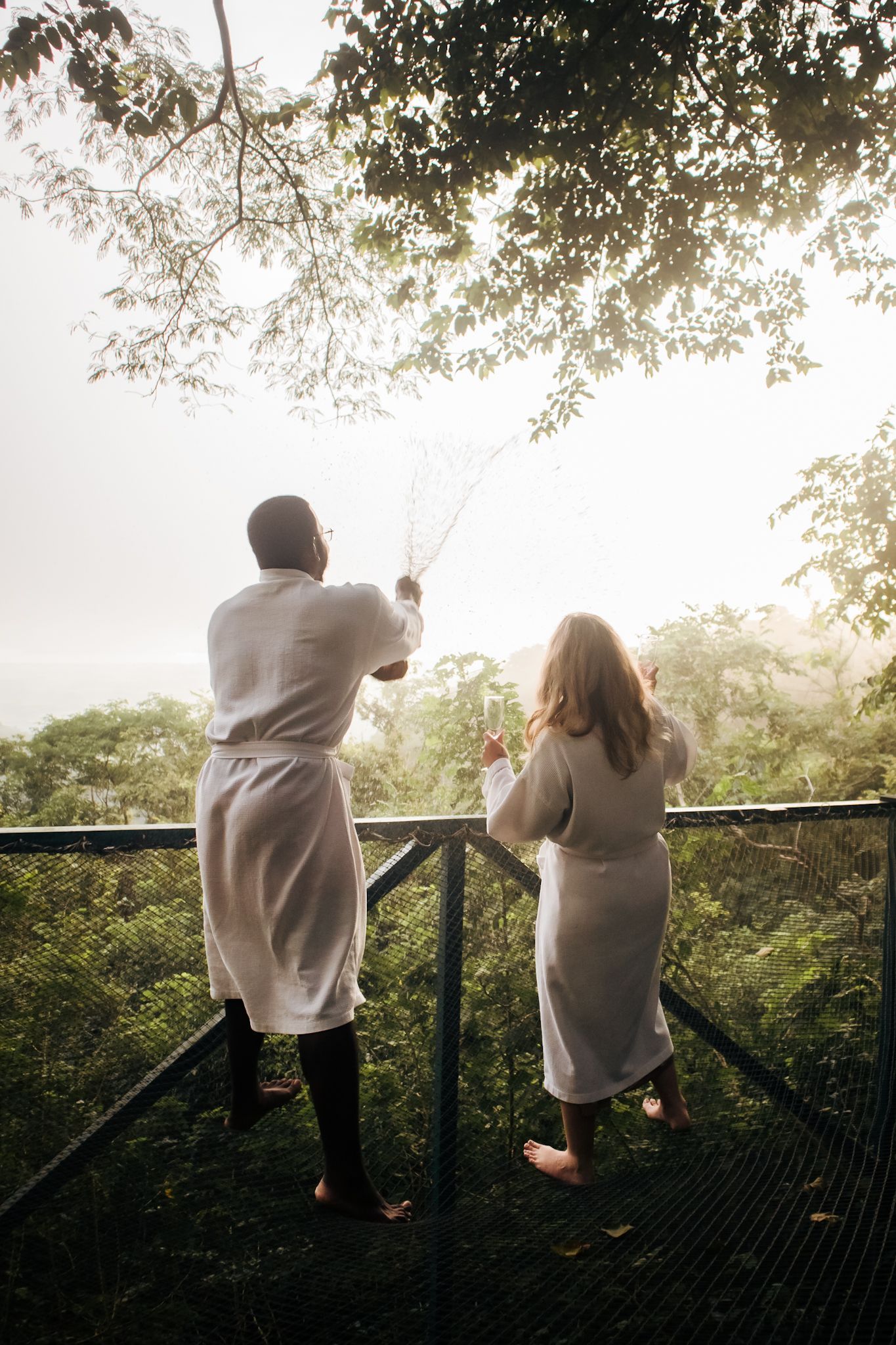 A man and a woman are standing on a balcony looking out over a forest.