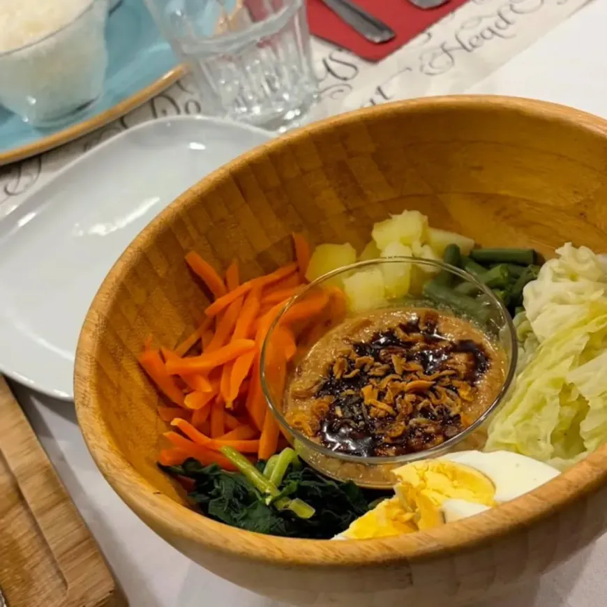 Bol de madera con bibimbap, verduras, huevo y salsa picante sobre la mesa de un restaurante.