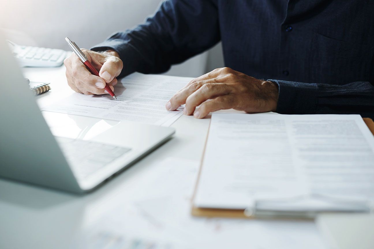Homme qui rédige sur une feuille avec un crayon rouge et un ordinateur
