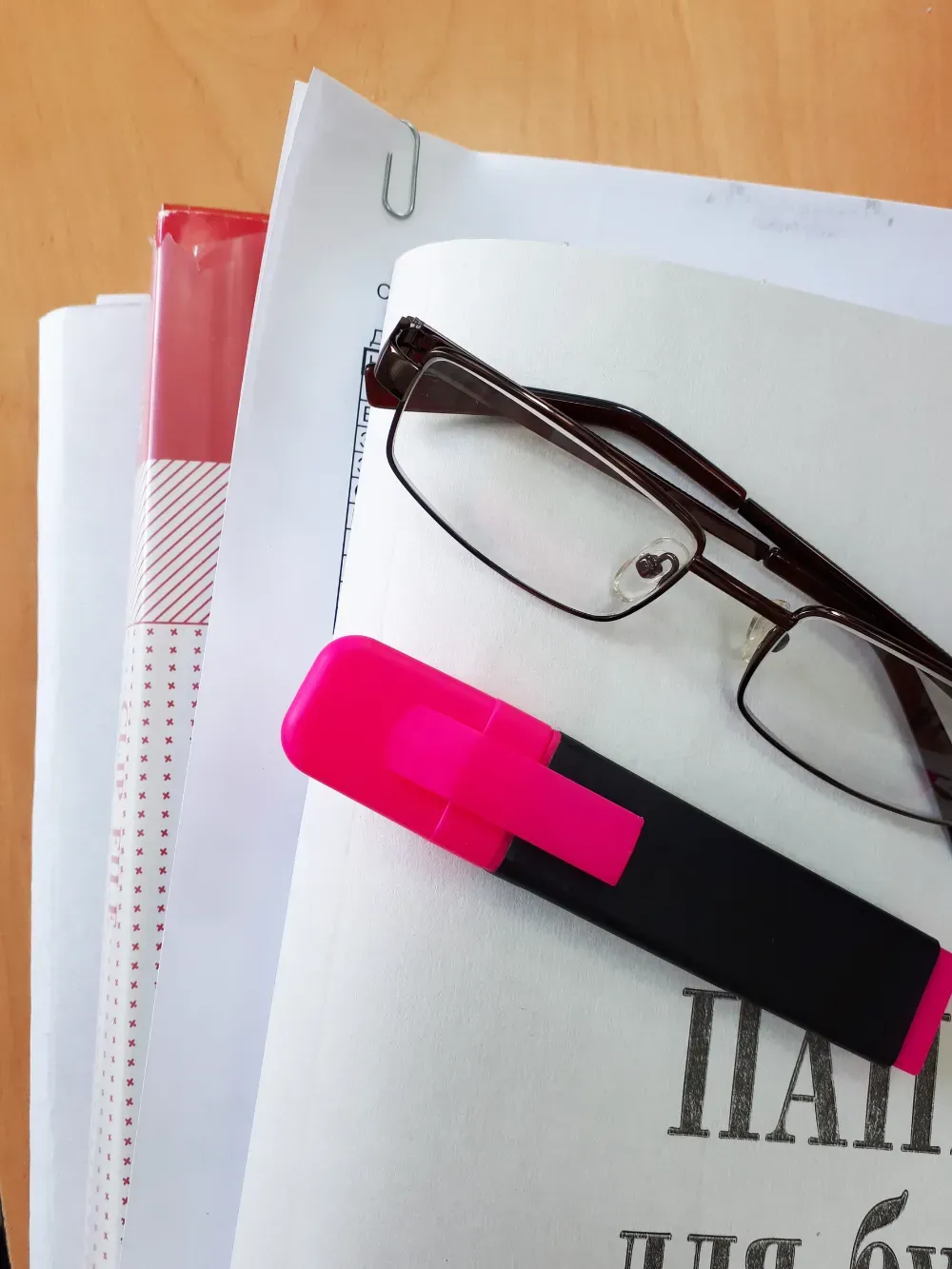 Un par de gafas con montura oscura y un resaltador rosa brillante sobre una pila de papeles blancos.