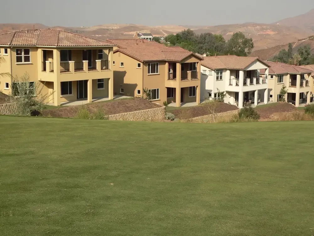 Una hilera de casas de estuco de color blanco y marrón con techos de tejas con vista a una gran colina verde y cubierta