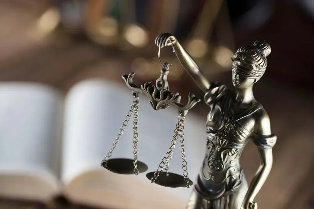 Una estatua metálica de la Dama de la Justicia sosteniendo una balanza, colocada frente a un libro abierto