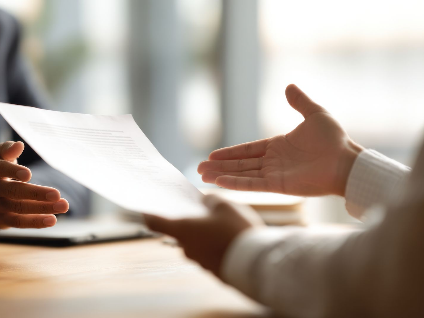Des mains se passent un document par-dessus une table ; contexte de bureau.