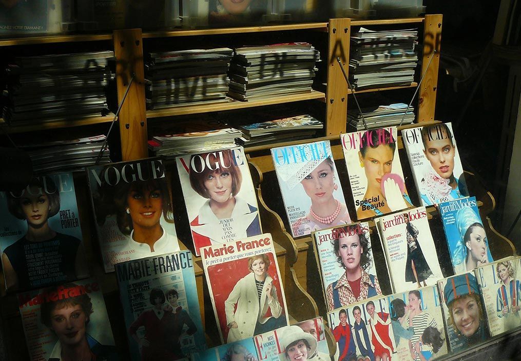 Un présentoir en bois à plusieurs niveaux contient divers magazines de mode vintage, dont plusieurs exemplaires de Vogue.