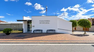 Edificio blanco moderno con el rótulo «TEACHERS HOME», bancos y un jardín delantero de estilo desértico bajo un cielo azul.