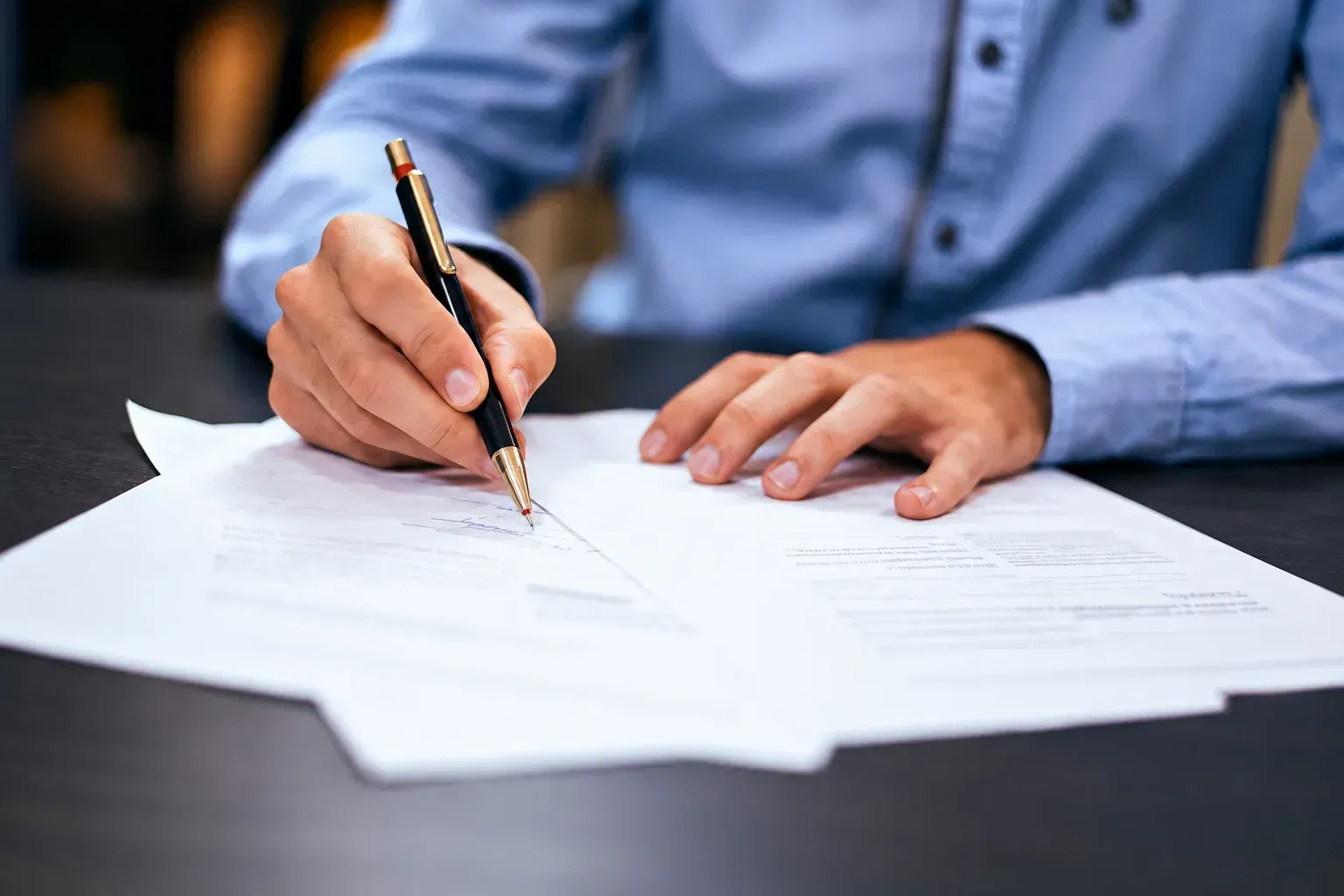 Persona firmando documentos con un bolígrafo en un escritorio