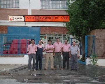 Un grupo de hombres parados frente a un edificio que dice auto recambios recases