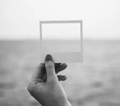 Una mano sostiene un marco de fotos transparente contra un paisaje gris borroso.