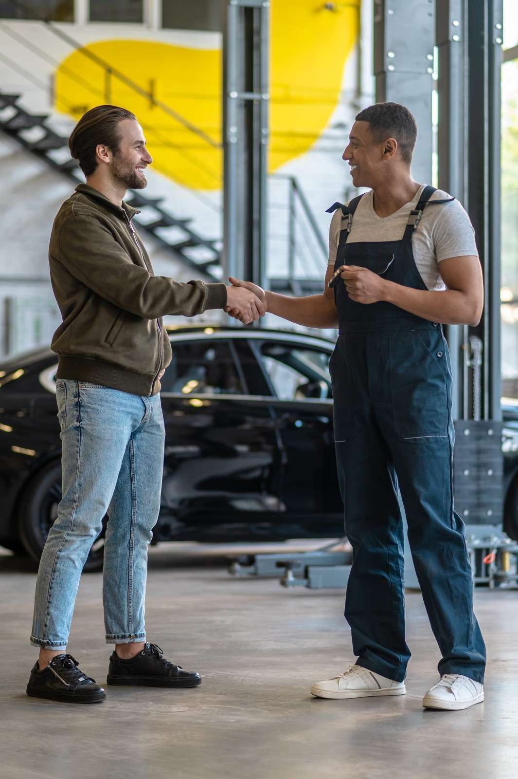 Un cliente y un mecánico se dan la mano dentro de un taller después de que le hayan hecho la revisión al coche.