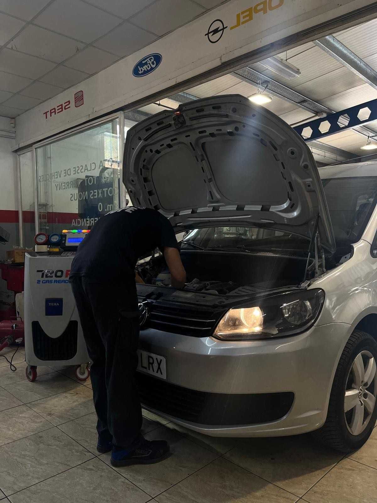 Un cliente y un mecánico se dan la mano dentro de un taller después de que le hayan hecho la revisión al coche.