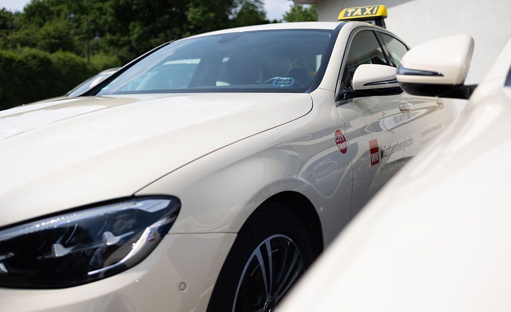 Ein weißes Auto mit einem Taxischild darauf ist neben einem anderen Auto geparkt.