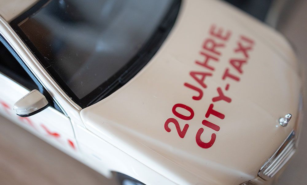 Ein weißes Auto mit roter Schrift, auf der steht 20 Jahre City-Taxi
