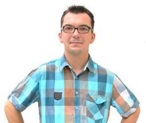 Ein Mann mit Brille und kariertem Hemd steht mit den Händen in den Hüften da.