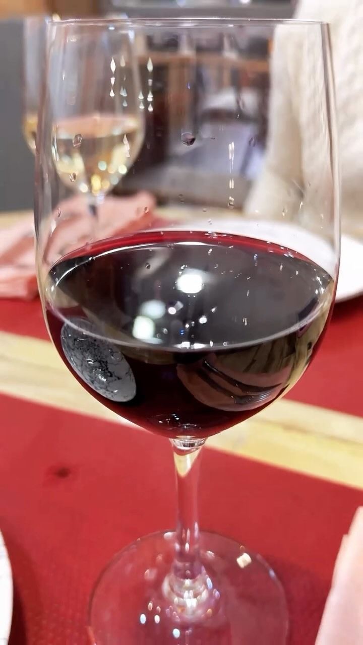 Una copa de vino tinto sobre una mesa roja con un restaurante desenfocado de fondo.