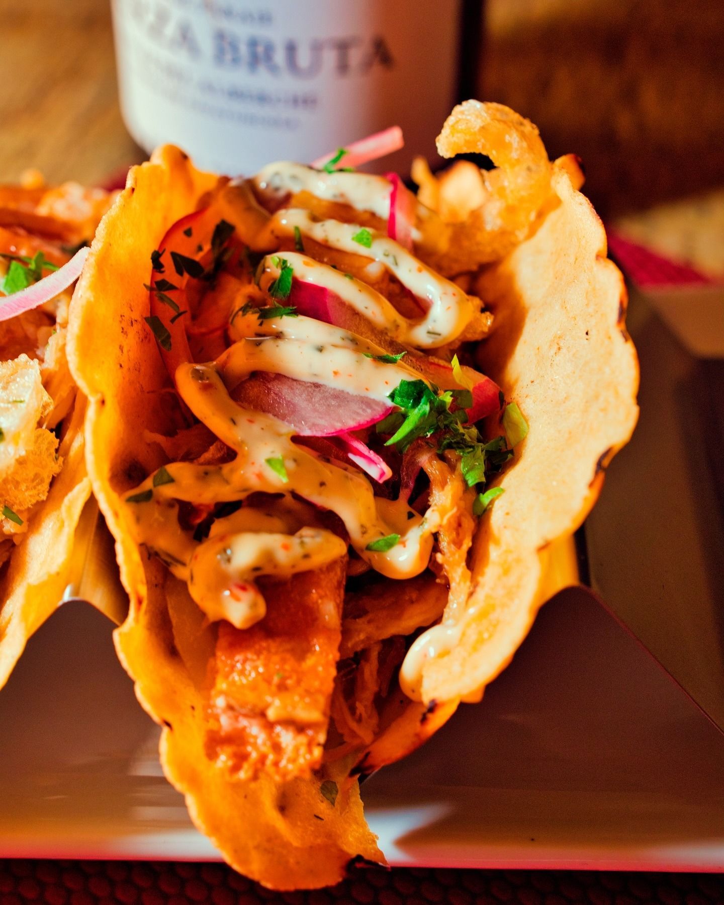 Tacos rellenos en un plato con tortilla naranja, carne sazonada, cebolla y cilantro, con salsa cremosa encima.