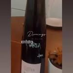 Botella de vino oscuro con etiqueta negra sobre una mesa en el interior.