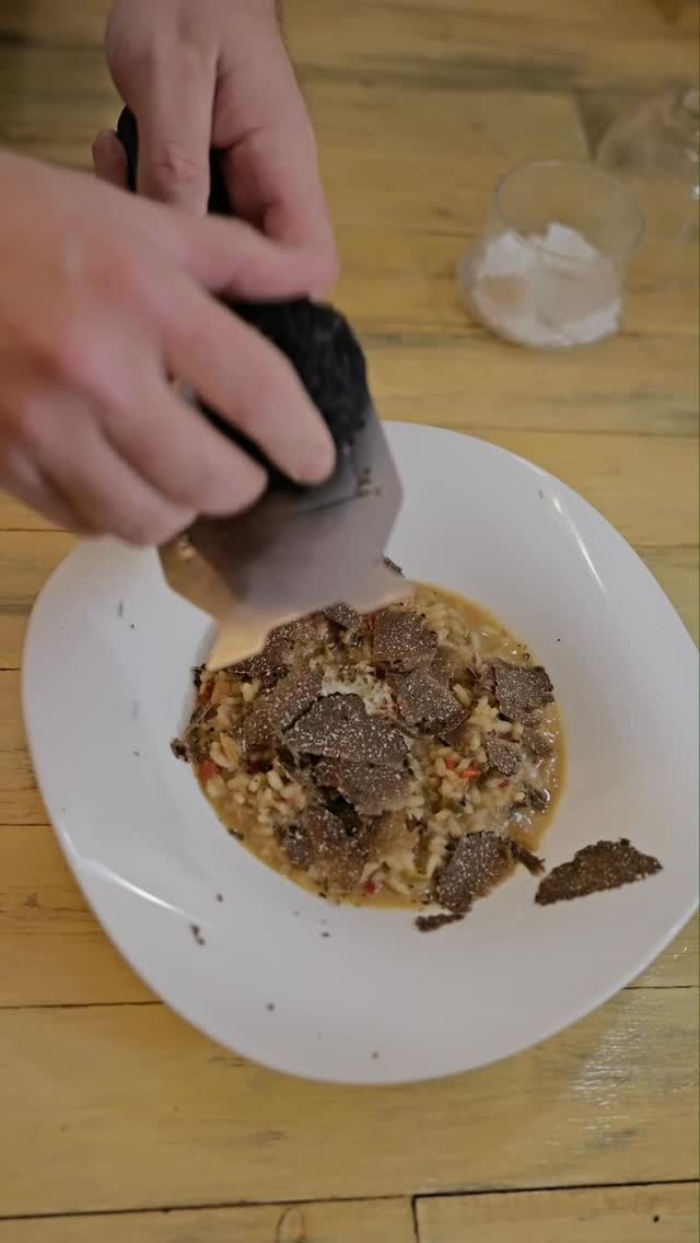 Manos cortando un plato dorado sobre un plato blanco en una mesa de madera.