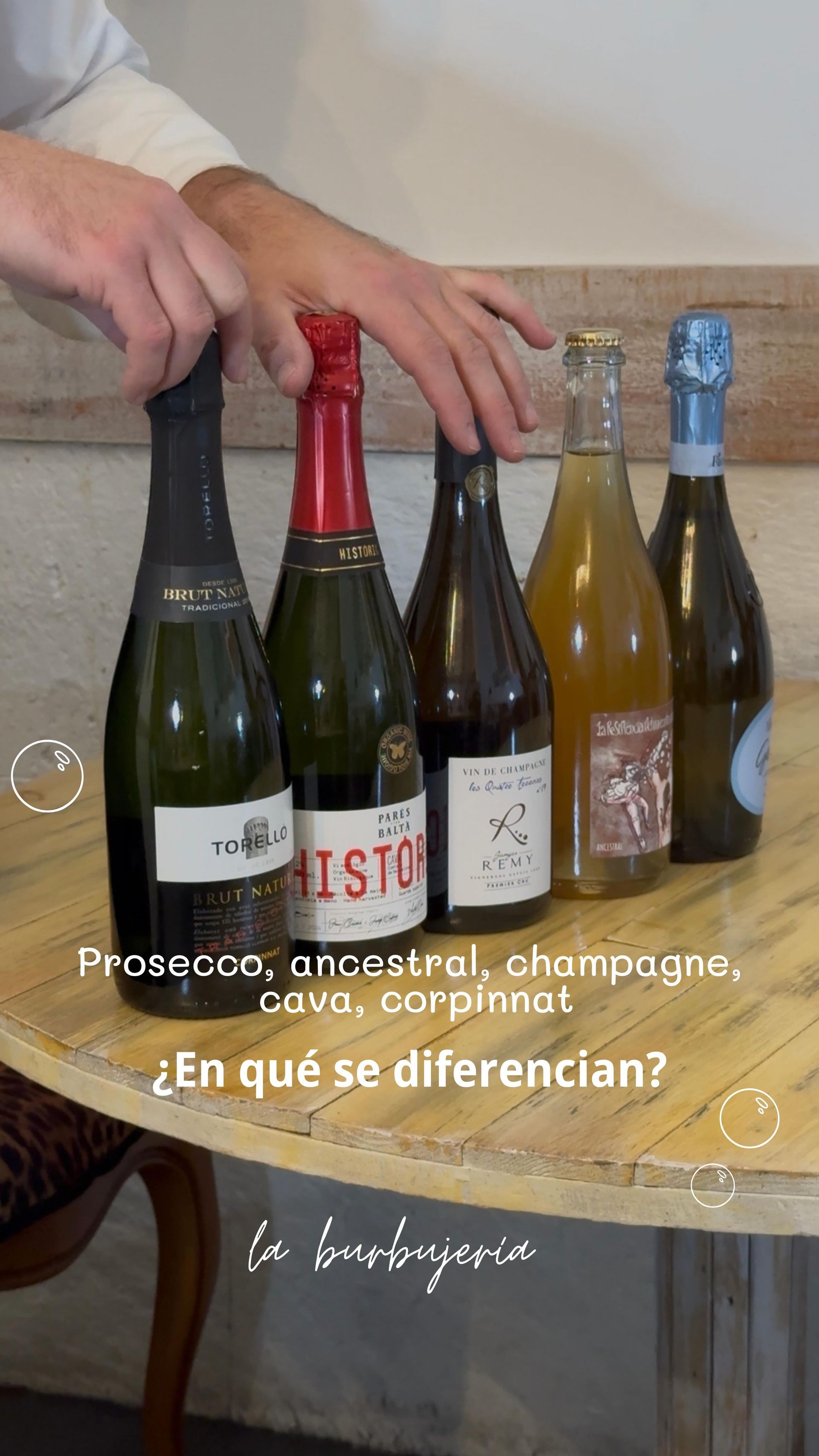 Manos señalando cinco botellas de vino sobre una mesa con texto en español sobre diferentes vinos espumosos.