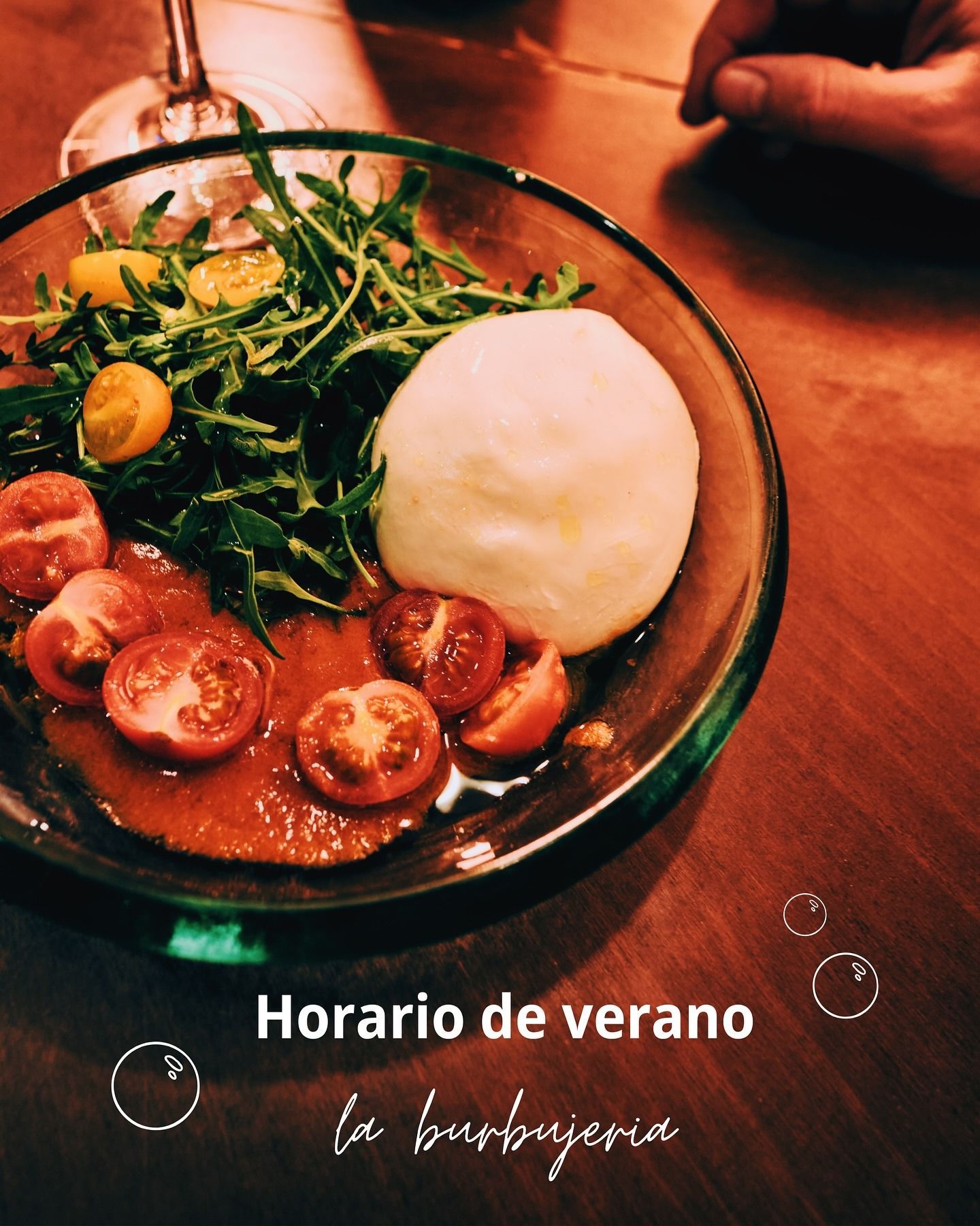 Plato de ensalada con burrata y tomates cherry en una mesa de madera, con texto “Horario de verano”