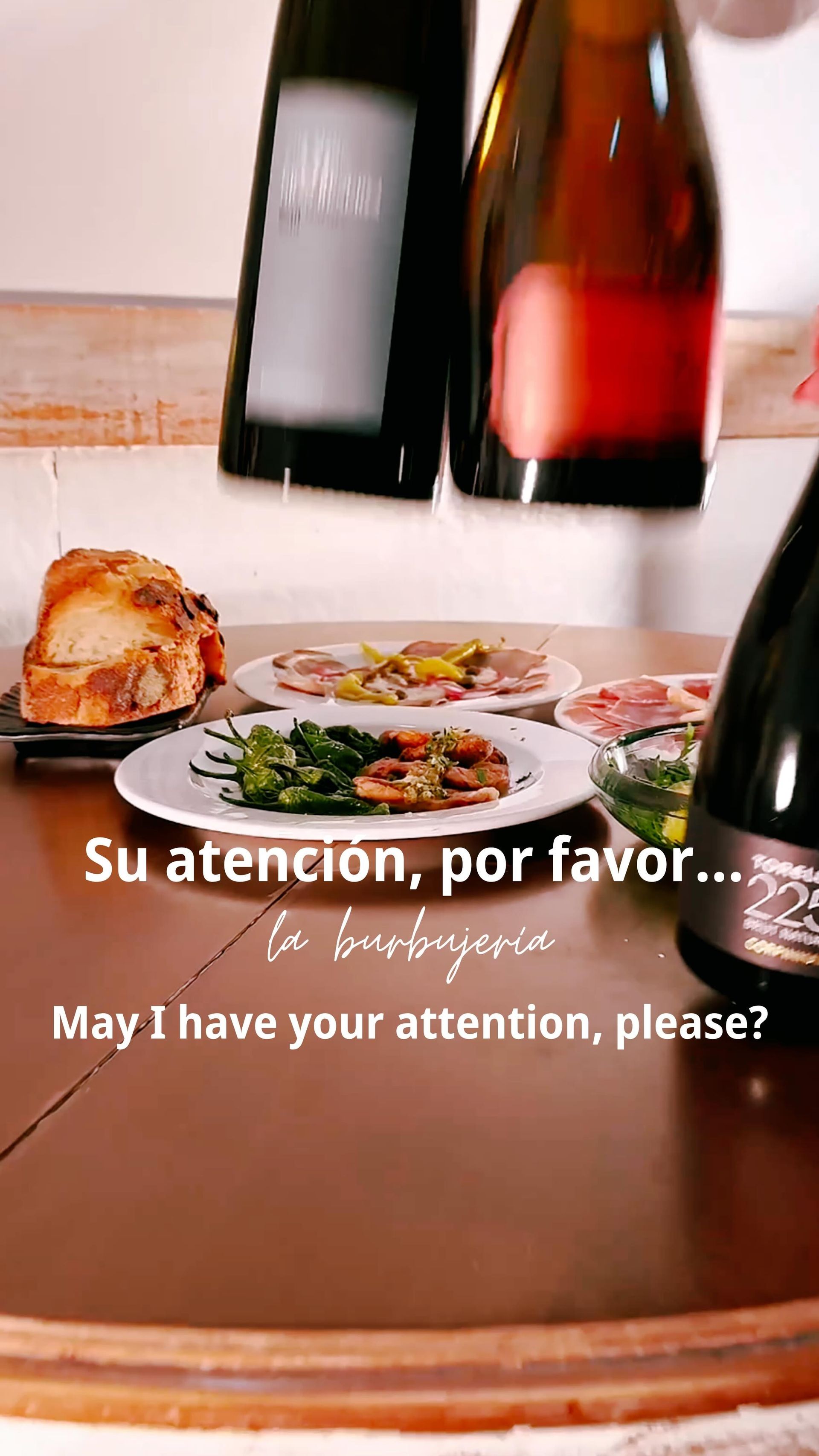 Mesa de restaurante con botellas de vino, un plato de comida y un texto que dice 