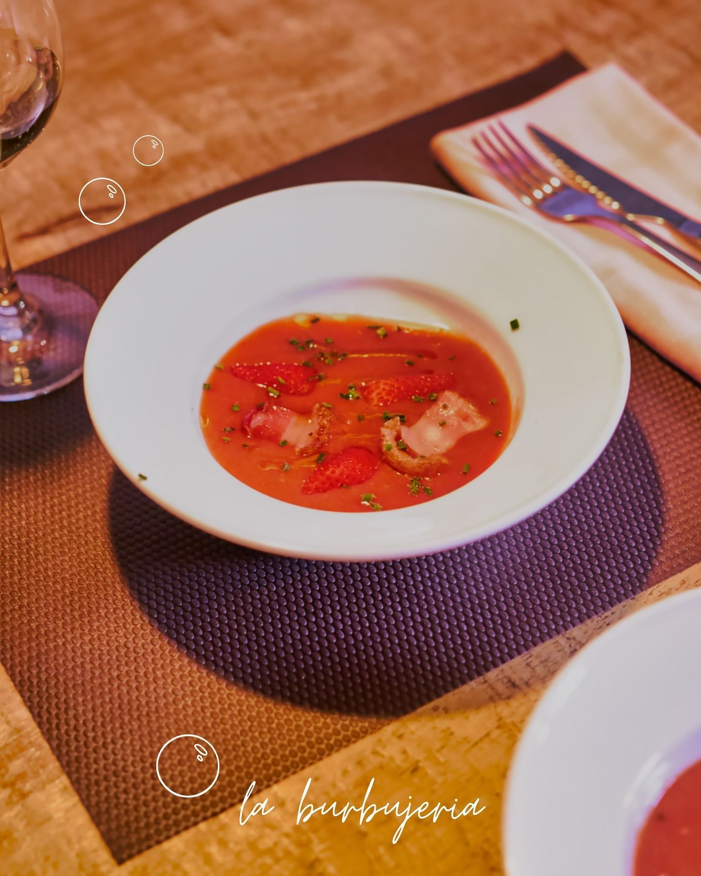 Tazón de sopa roja con guarnición sobre un mantel individual tejido, visto desde arriba en una mesa puesta.