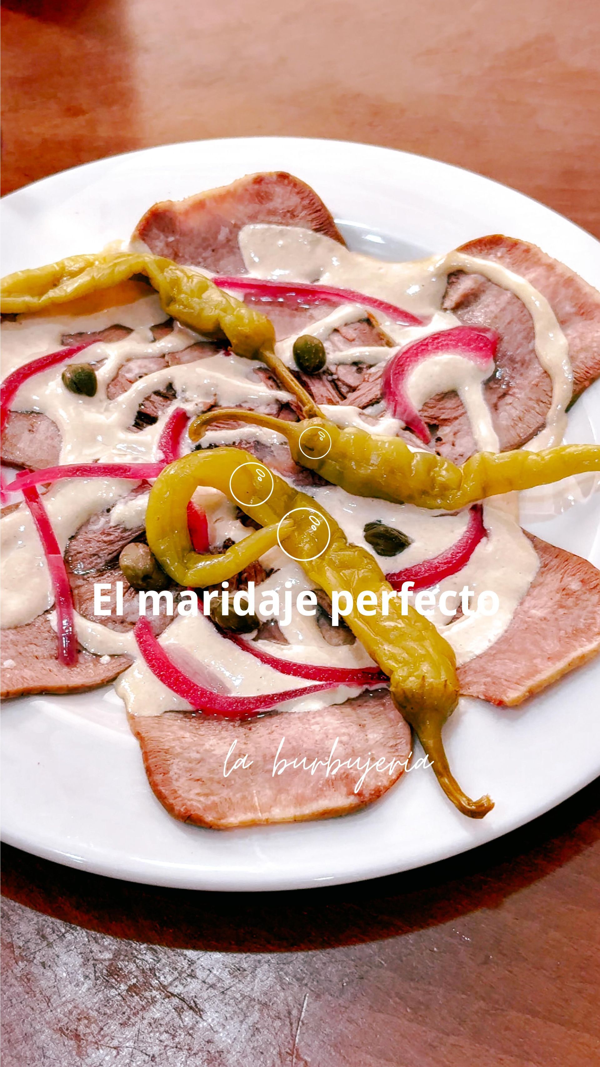 Carne en rodajas sobre un plato blanco con champiñones, cebolla roja y pimientos verdes sobre una mesa de madera.