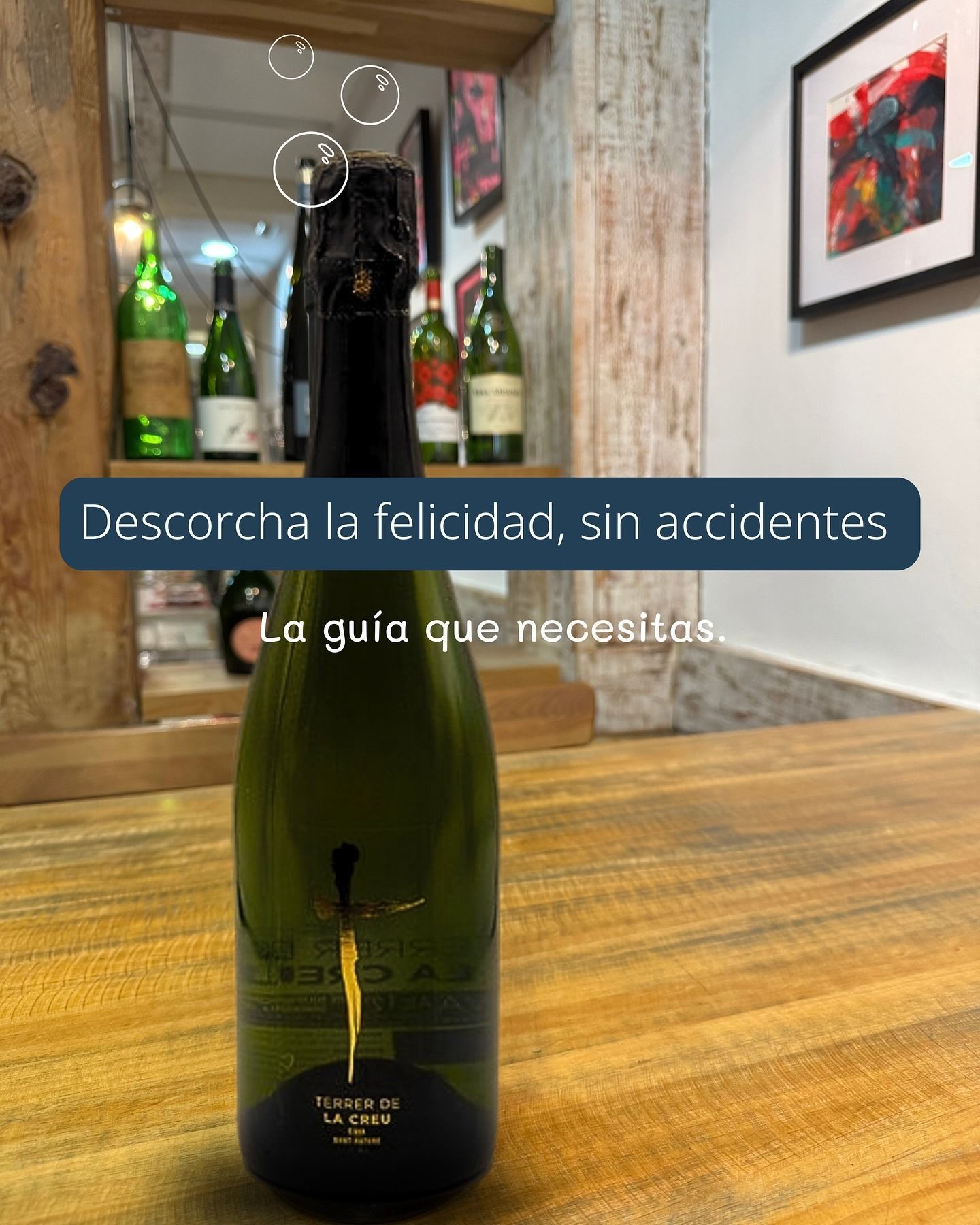 Botella de vino espumoso verde sobre mesa de madera, con texto promocional en español.